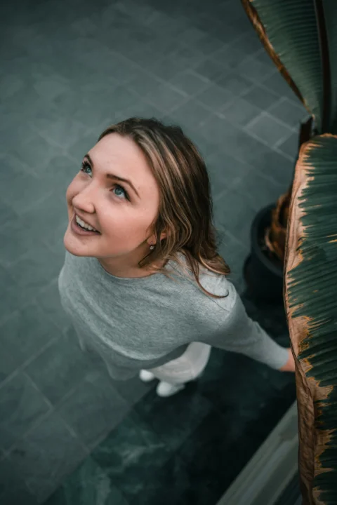 A woman in a grey long-sleeved shirt looking upward near a large leaf