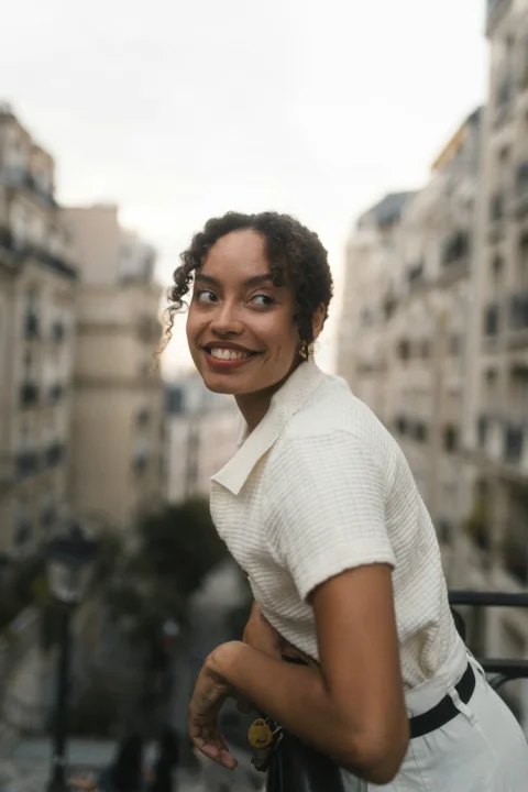 A woman in a white collared shirt leaning on a balcony in Paris