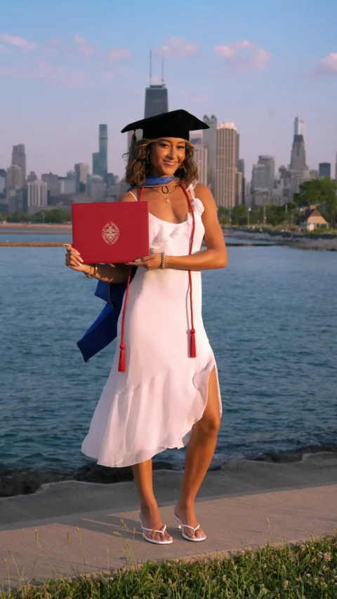 A woman in a graduation gown holding a laptop