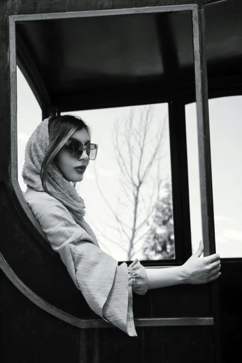 a woman wearing a scarf and sunglasses looking out a window