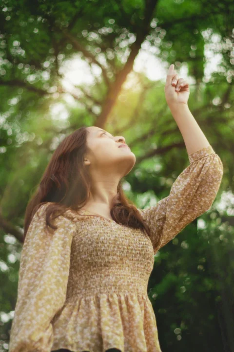 白天身穿米色针织毛衣的女子站在绿树旁