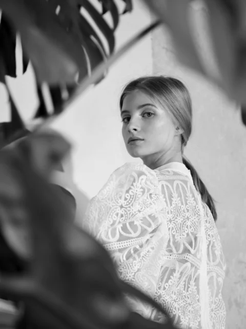 Young woman in white lace top peeking through leaves