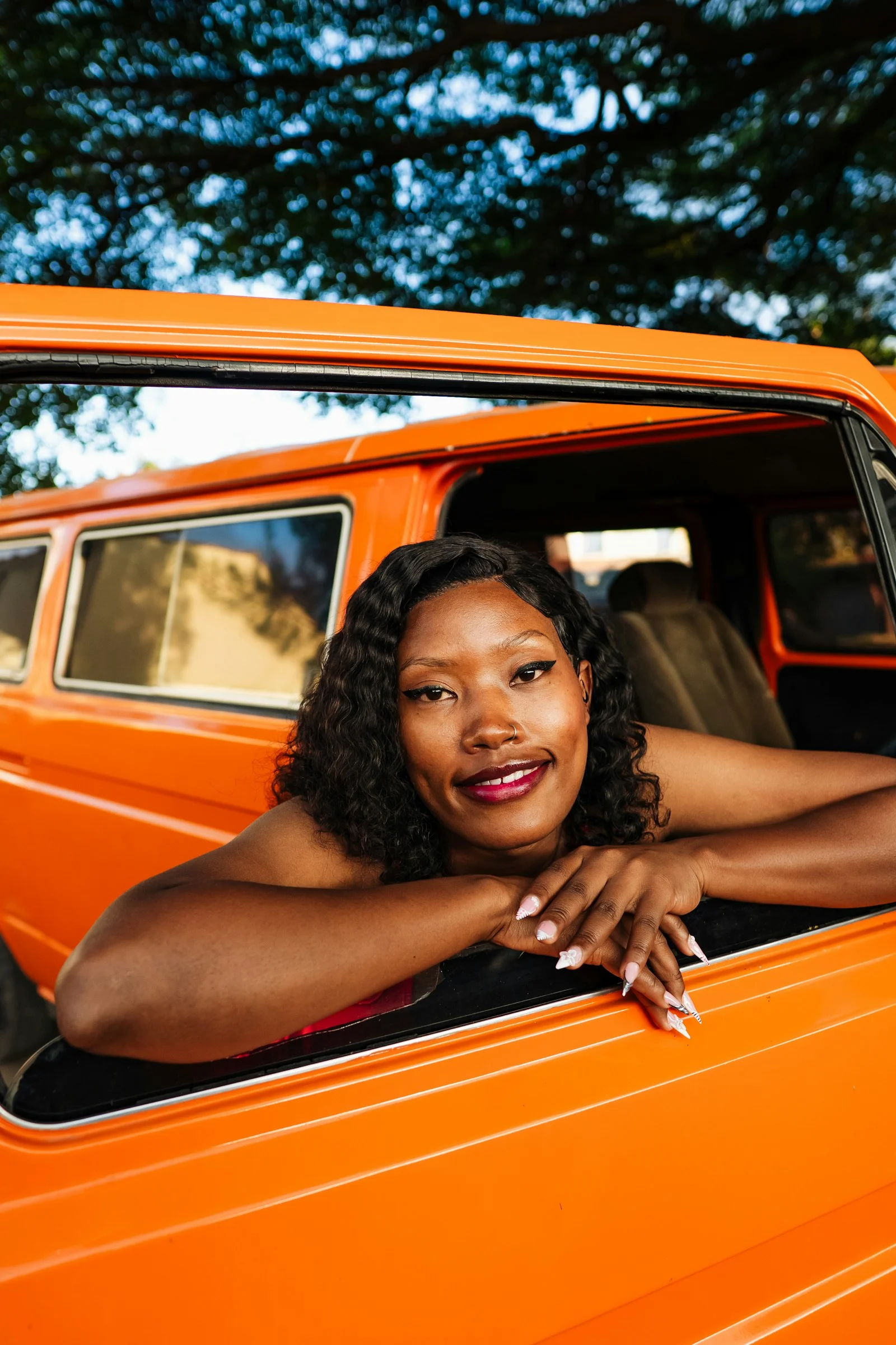 Woman leaning on orange van window smiling at sunset