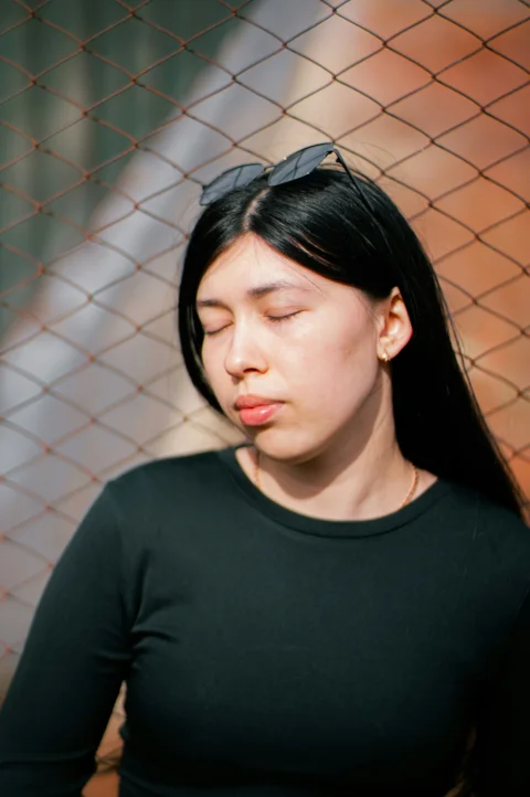 Woman with sunglasses closes her eyes near a fence