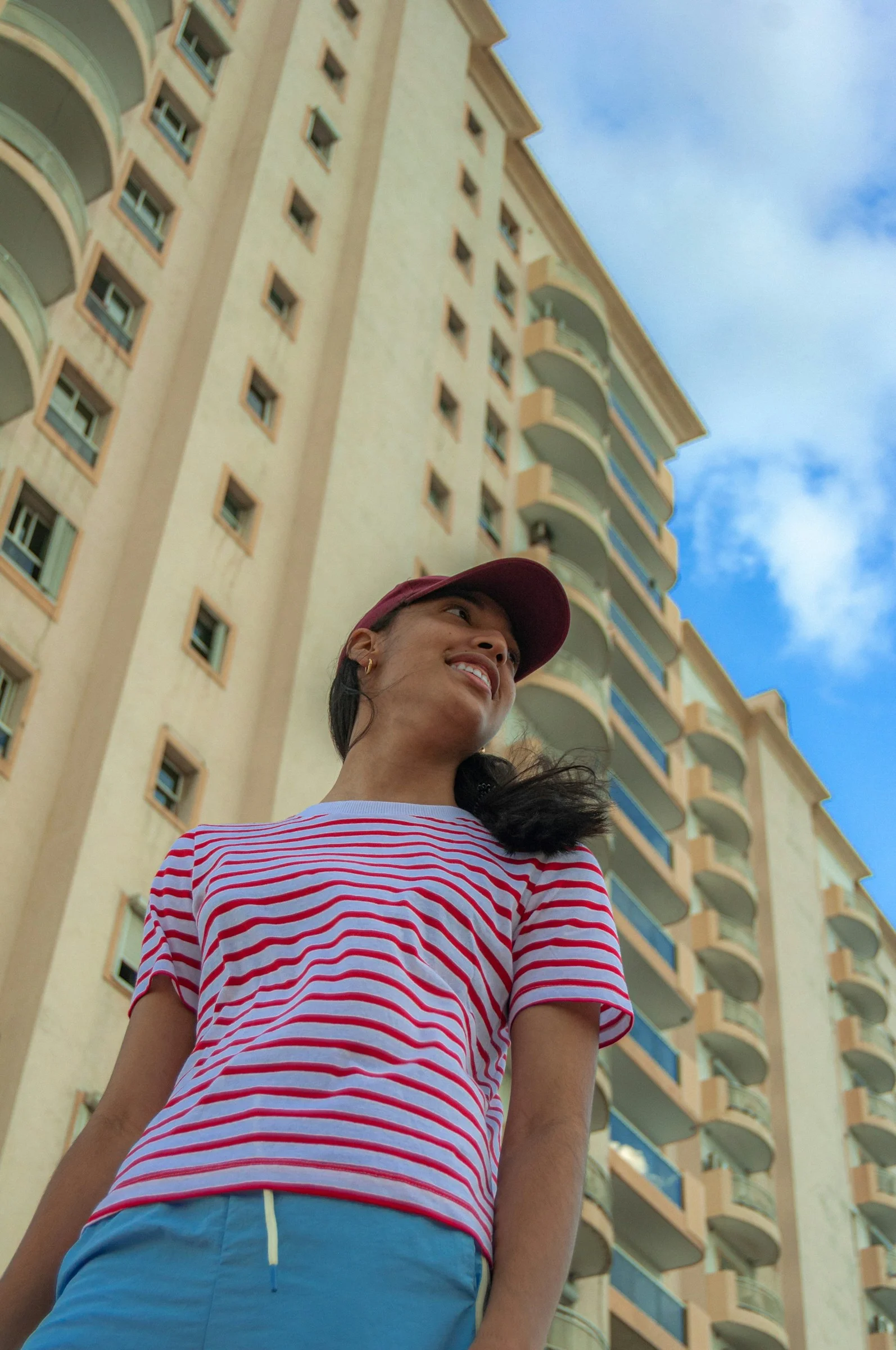 woman in white and red striped shirt and brown hat standing near brown concrete building during