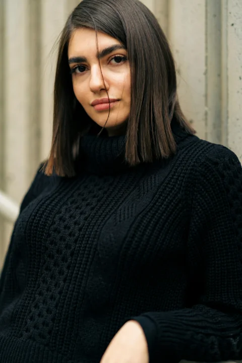 a woman in a black sweater leaning against a wall