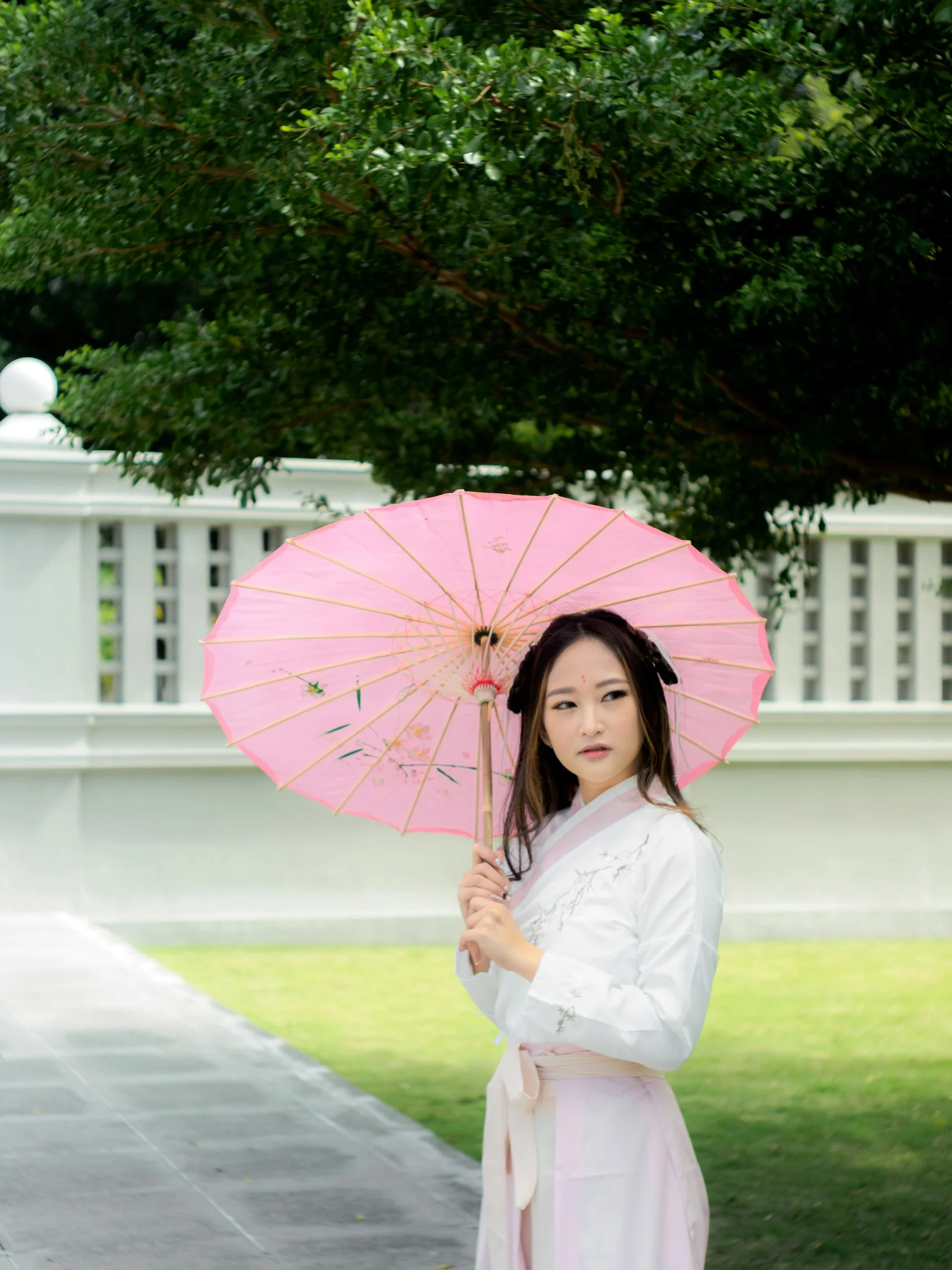 身穿白色连衣裙、手持粉色雨伞的女子