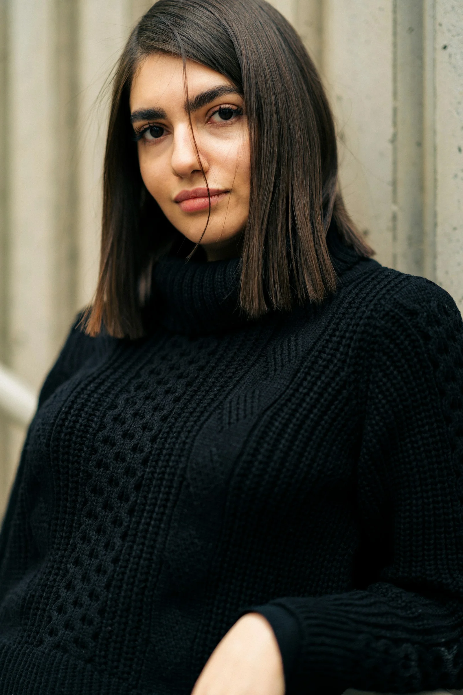 a woman in a black sweater leaning against a wall