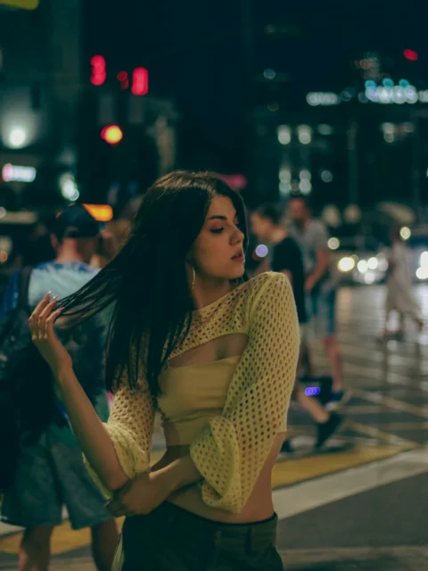 a woman standing on the side of a street at night