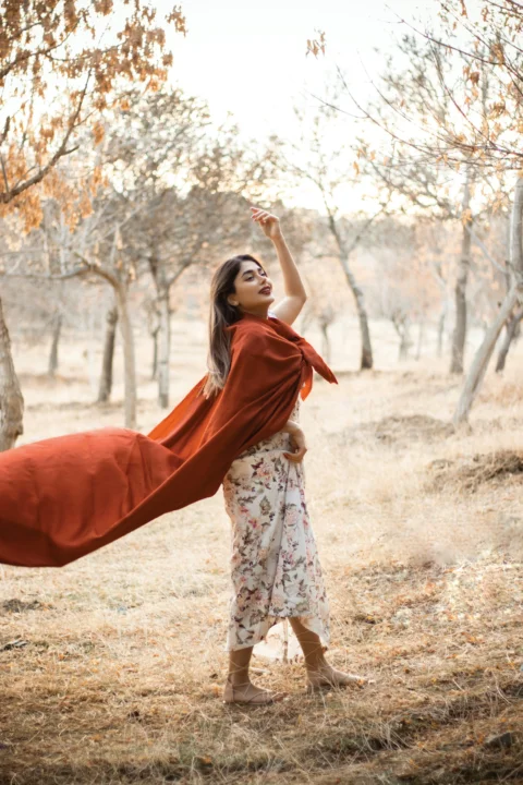 a woman standing in a field holding a red blanket